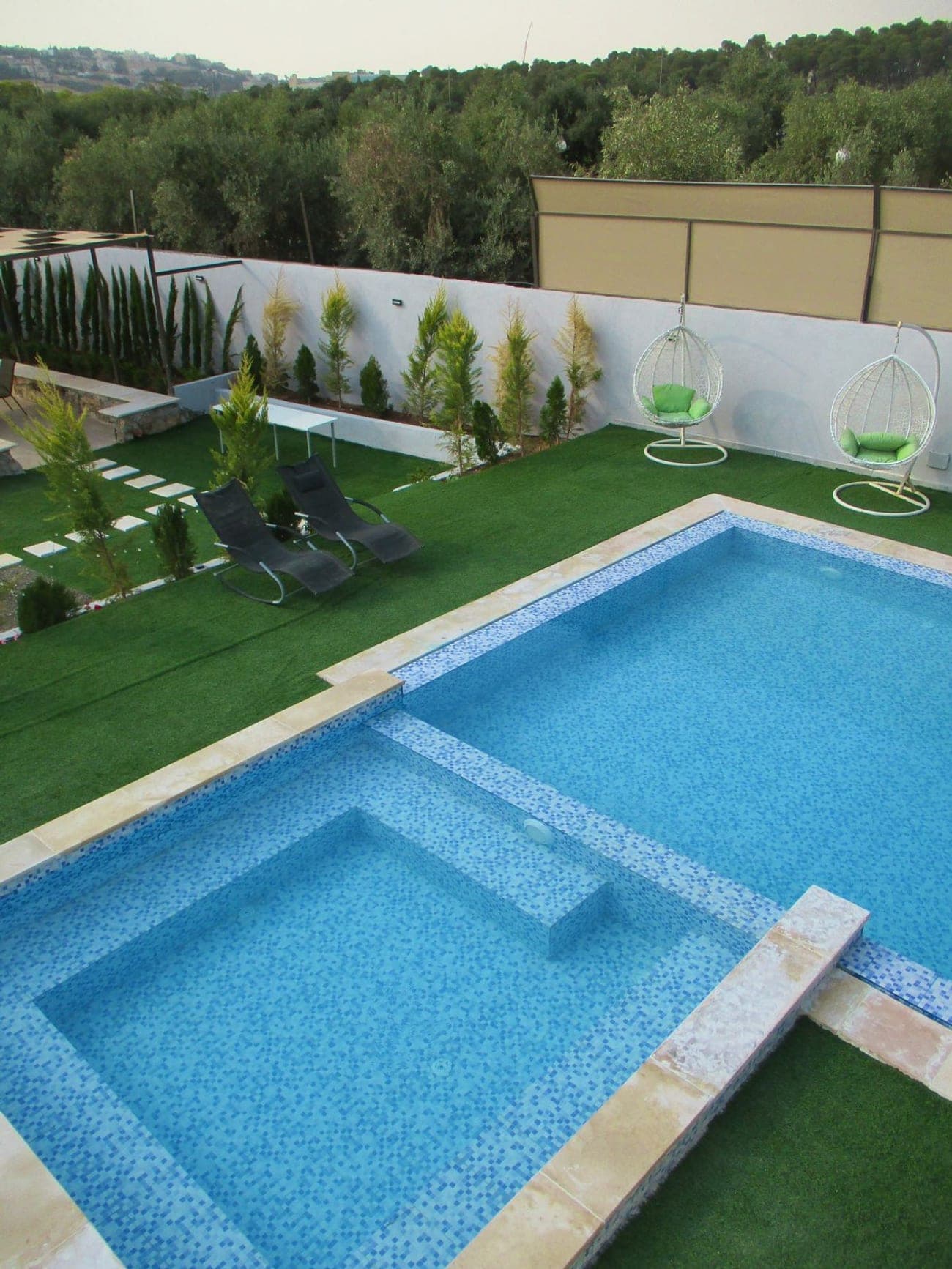 Villa 101 pool at dusk with hanging chairs and cypress trees